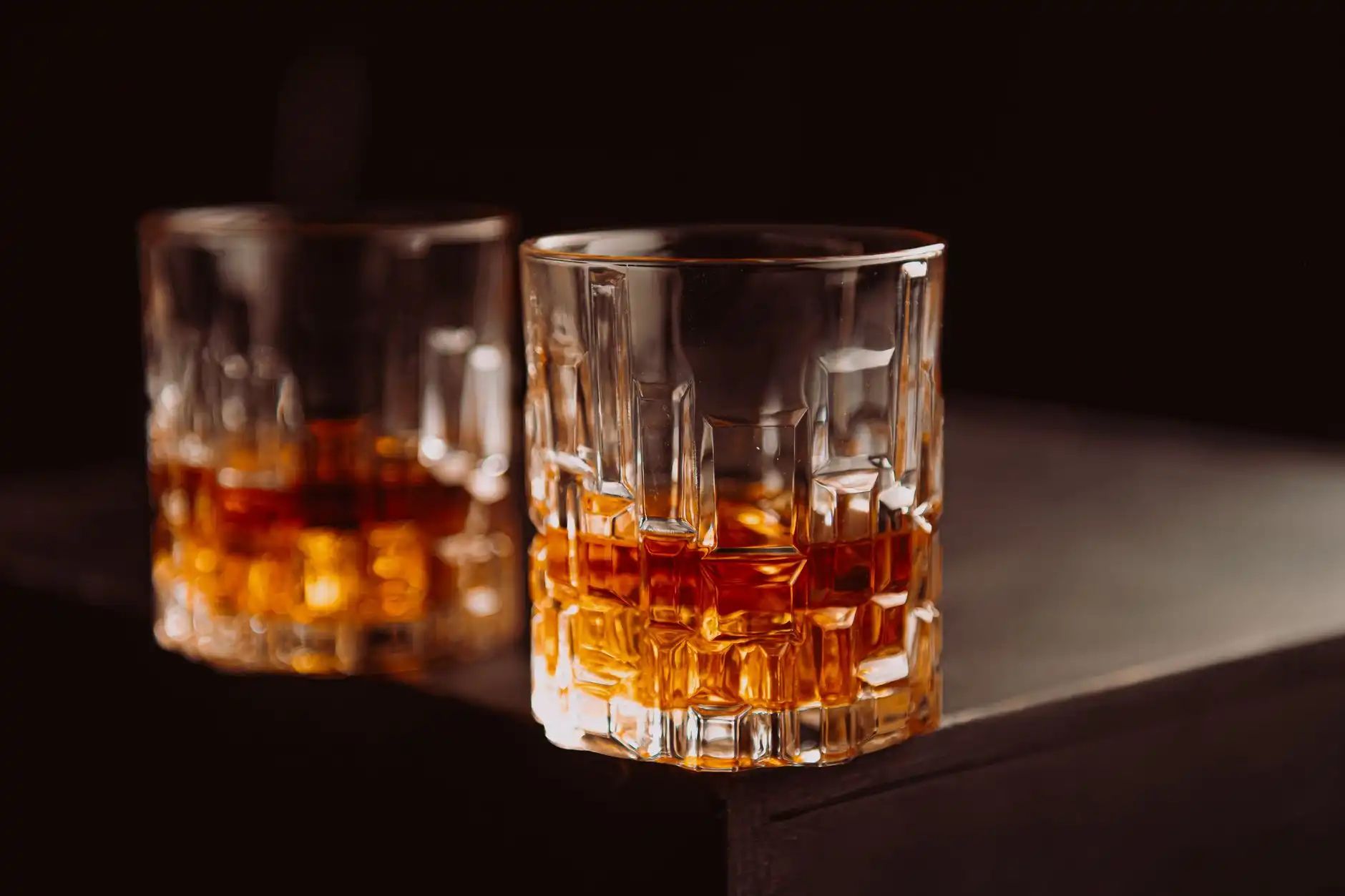 Two glasses of amber rum on a dark wooden bar
